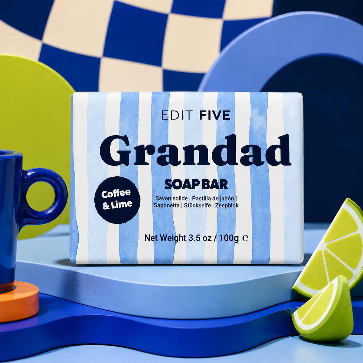A boxed soap bar labeled 'Grandad SOAP BAR' with blue-and-white vertical stripes, placed on a blue pedestal with coffee and lime props. The visible brand is EDIT FIVE. Grandad coffee and lime soap bar, handmade in England with 100% natural essential oil, a gentle exfoliating texture and gift-ready packaging—perfect for birthdays, Father’s Day or Christmas.