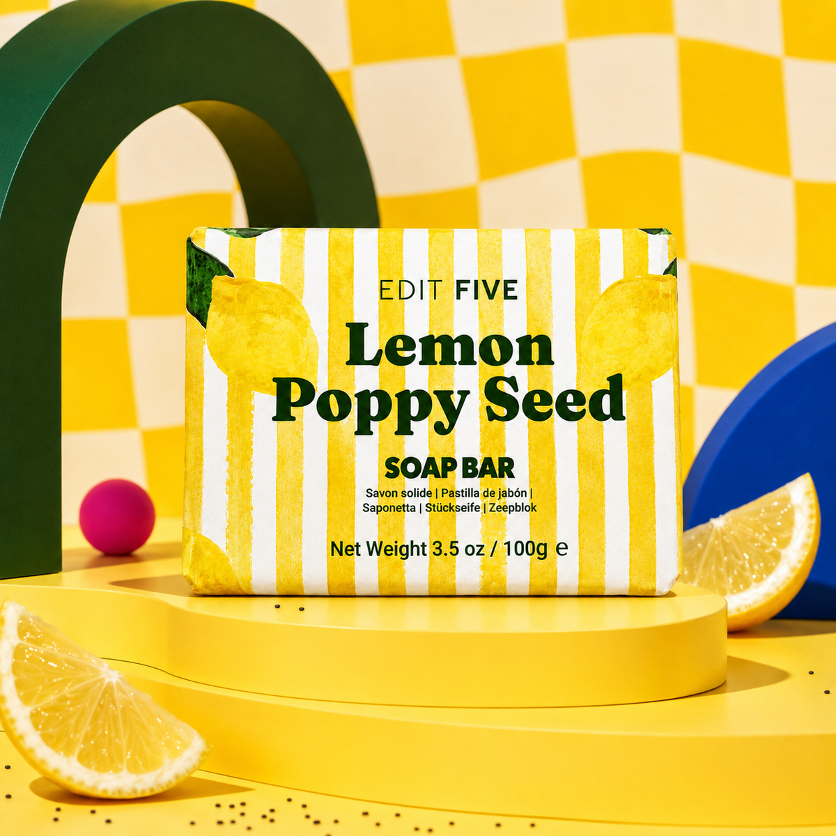 A lemon poppy seed soap bar by Edit Five, presented in its yellow and white striped packaging on a yellow pedestal, surrounded by decorative yellow and green props. Lemon poppy seed soap bar, handmade in England with 100% natural lemon essential oil, gently exfoliating poppy seeds and bright gift-ready packaging for refreshing daily skincare.