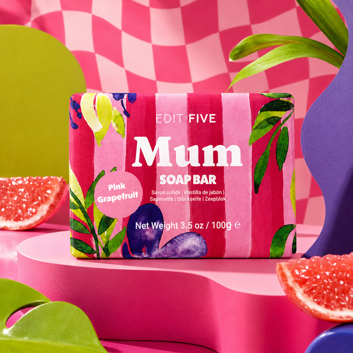 A pink striped soap bar package labeled 'EDIT FIVE Mum SOAP BAR' and 'Pink Grapefruit,' styled on a pink pedestal with grapefruit slices and colorful abstract shapes in the background. Mum pink grapefruit soap bar, handmade in England with 100% natural essential oil and blush-toned gift-ready packaging—a thoughtful Mother’s Day, birthday or Christmas gift for Mum.